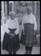 Paní Anna Jankech (malá) a pí Katerina Valová ze Stráže u Krahovan (velká), prodavačky výšivek před Národopisným museem v čepicích (pohled ze předu)