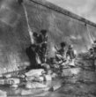 Ženy s děti se myjí a perou prádlo ve vodě vytékající z potrubí v kamenné zdi