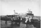 Maják a větrný mlýn na břehu, ve vodě chlapci s dobytčetem