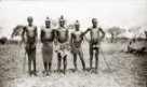 Skupina mužů kmene Kamčuru (Ačoli), někteří mají na hlavě malé homolovité  čepičky