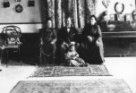 Baron H.Descallar a dvě ženy sedící na pohovce v pokoji, u nohou jim sedí arabské dítě s kočkou