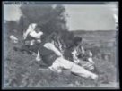 Skupina žen v krojích a muž sedící na trávě