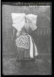 Mladá žena v tradičním svátečním kroji, v čepci s velkou plátěnou holubicí, pohled zezadu