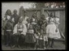 Skupina žen, dívek, mužů a dětí - rodina v polosvátečních krojích, před vraty statku