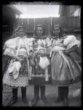 Tři děvčata ve svátečních krojích u dřevěných vrat, stojící, pohled zpředu