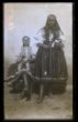 Dvě ženy, starší stojící - v šátku uvázaném pod bradu, mladší sedící - s účesem staženým do týlu