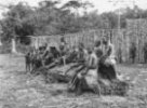 Skupina vesničanů sedících na kmeni před ohradou, Bambuti